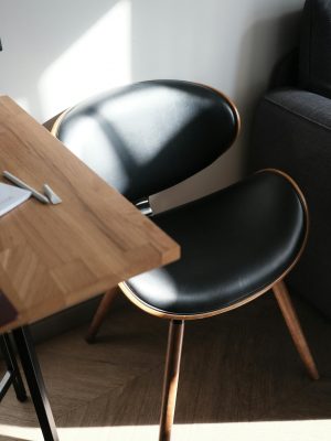 Contemporary black chair beside wooden desk illuminated by natural sunlight indoors.