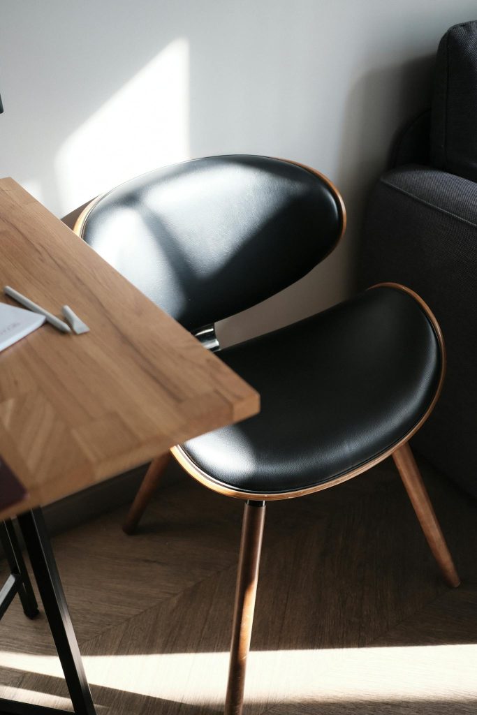 Contemporary black chair beside wooden desk illuminated by natural sunlight indoors.